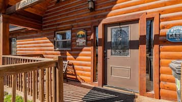 A wooden log cabin with a front door, a bench, and a welcome sign.