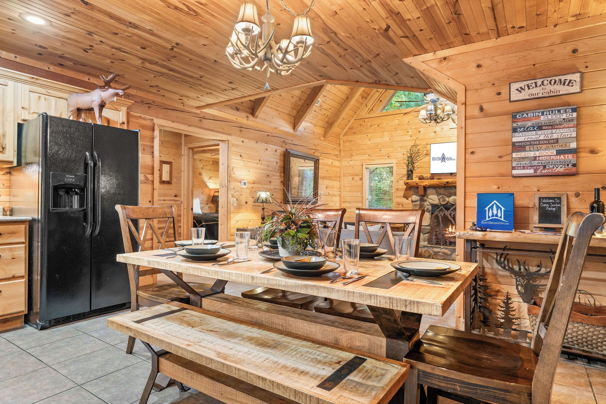 A cabin interior with a wooden dining table, benches, a black refrigerator, and a chandelier.