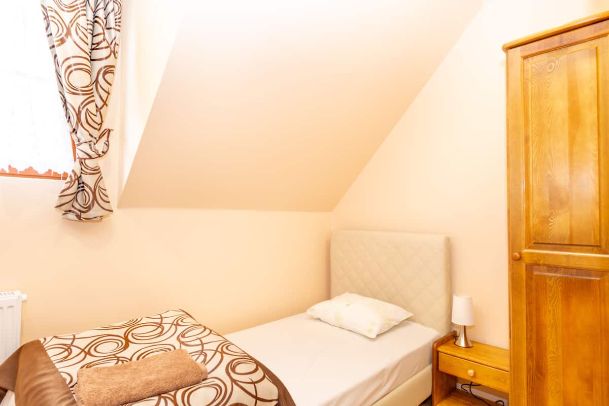 Ein Schlafzimmer mit einem Bett, einem Nachttisch, einem Holzschrank und einem Fenster mit gemusterten Vorhängen.