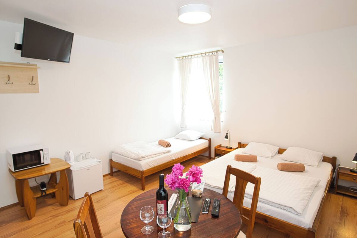 Ein Hotelzimmer mit zwei Betten, einem Fernseher, einer Mikrowelle, einem Tisch mit Blumenvase und einem Vorhangfenster.