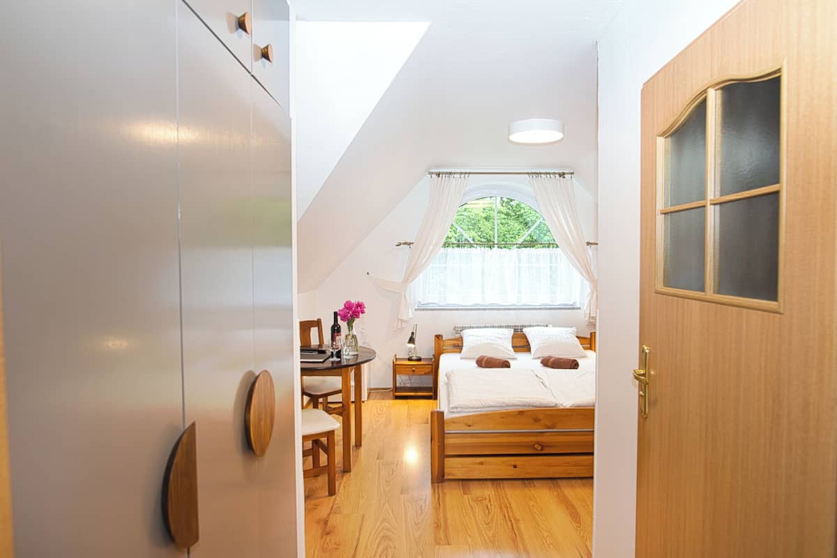 Ein Schlafzimmer mit einem Holzbett, einem kleinen Tisch mit Stühlen, einem Fenster mit Vorhängen und einer Tür mit Glasfenster.