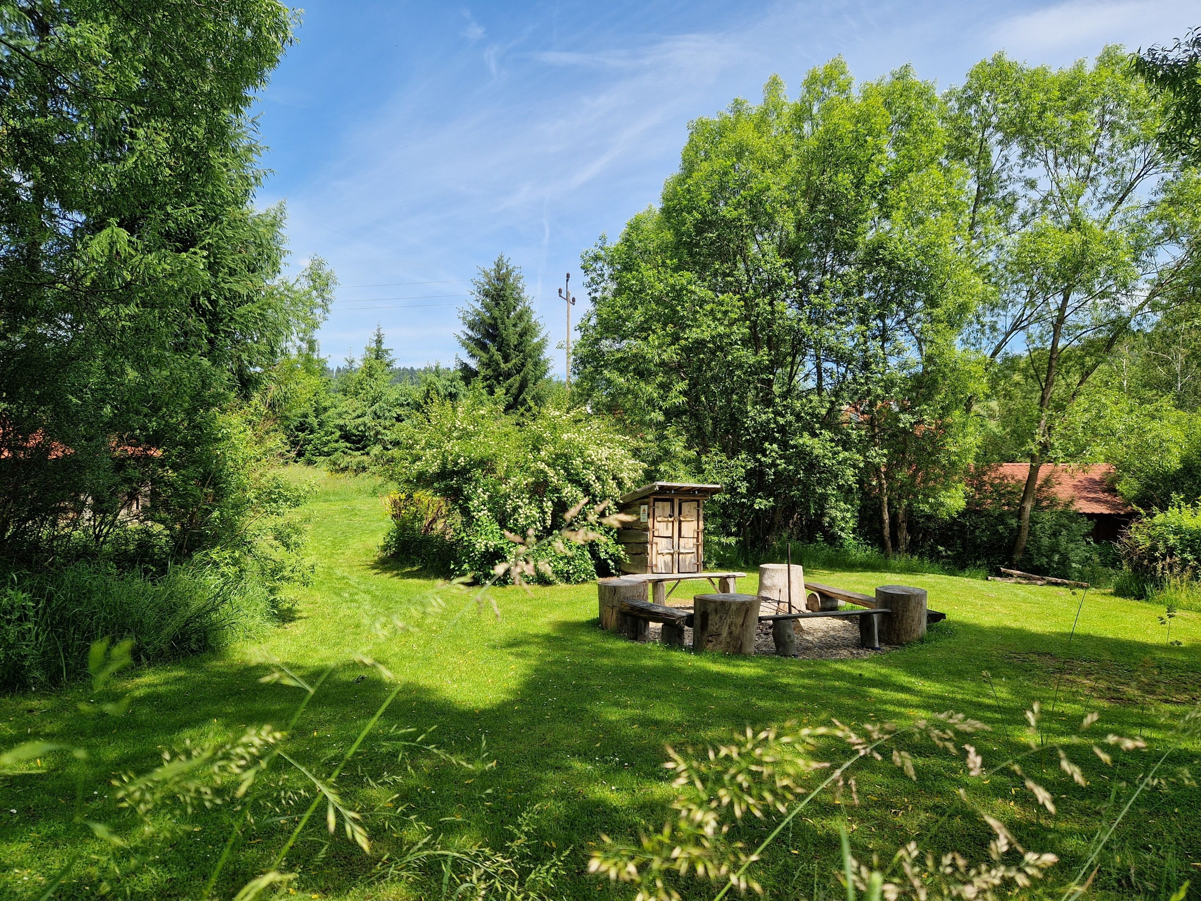 A rustic outdoor seating area with a wooden structure, surrounded by lush greenery and trees.