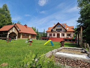 A large house with a red roof, a wooden cabin, and a grassy yard with playground equipment. - Gosciniec Pieciu Stawow (Ustrzyki Dolne)