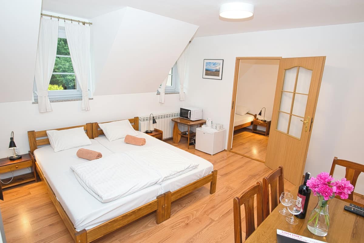 Ein Schlafzimmer mit einem hölzernen Bett, einem kleinen Tisch mit Flasche und Gläsern sowie einem Stuhl.