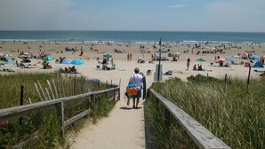 A sandy beach path leading to the sea with beachgoers and umbrellas.