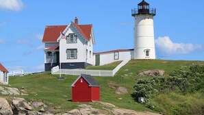 A lighthouse and a white house with a red roof on a grassy hill.