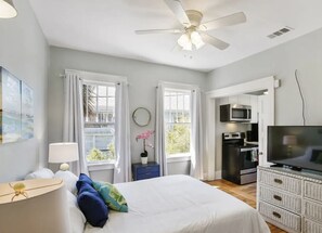 Une chambre avec un lit, un ventilateur de plafond, une télévision, un four à micro-ondes et un petit coin cuisine.