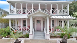 A two-story house with a porch, a pink door, and white railings.