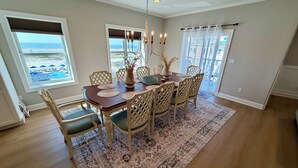 A dining area with a wooden table, six chairs, a chandelier, and a view of the ocean through large windows. - Beach Block End Unit with Ocean Views From All Rooms!! (Wildwood Crest)
