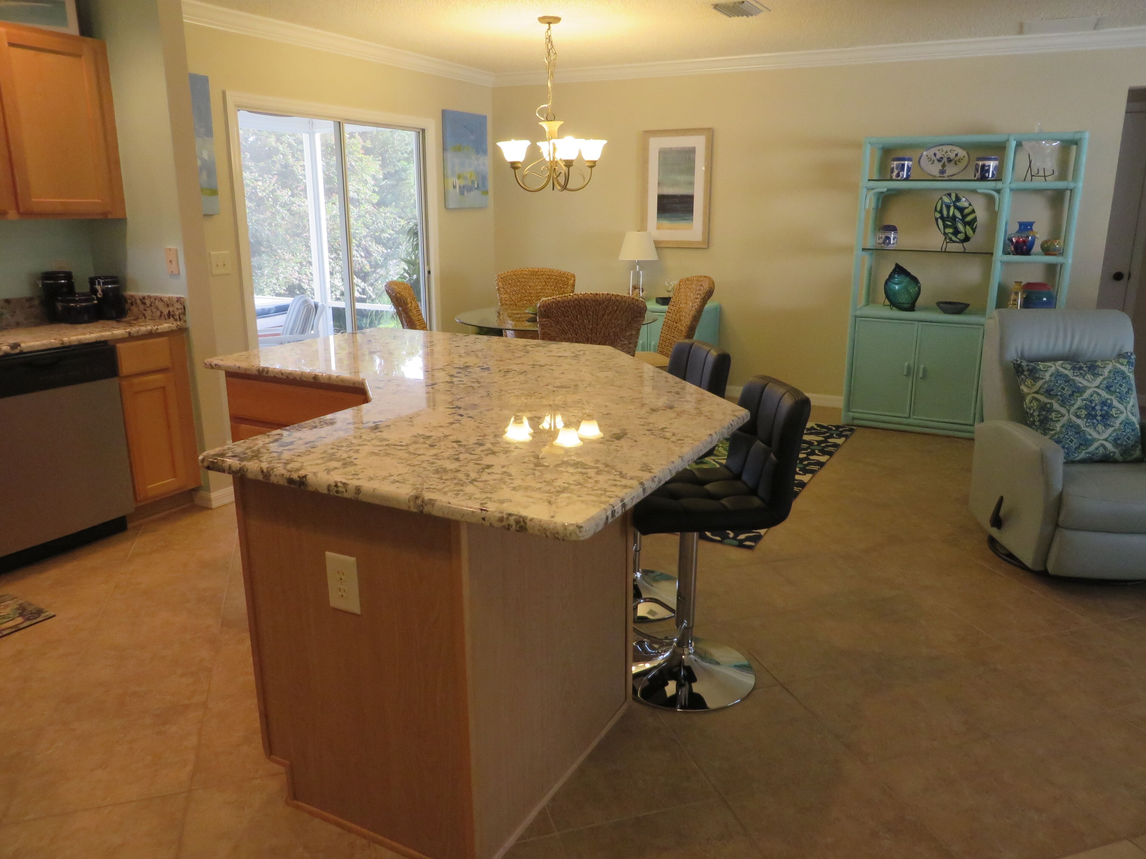 A kitchen with a central island, bar stools, a dining area with chairs, a teal cabinet with decorative items, and a chandelier.