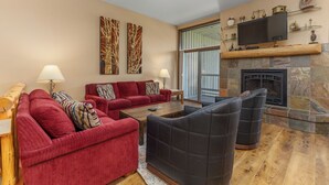A living room with a red sofa, black armchairs, a wooden coffee table, and a stone fireplace. - Short Walk to Slopes, Private W/D + Pool & Hot Tub (Steamboat Springs)
