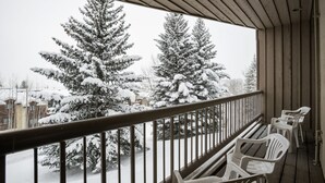 A balcony with a metal railing, white plastic chairs, and snow-covered trees in the background. - Short Walk to Slopes, Private W/D + Pool & Hot Tub (Steamboat Springs)