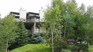 A two-story building with a balcony on the second floor, surrounded by lush greenery and a well-maintained lawn. - Short Walk to Slopes, Private W/D + Pool & Hot Tub (Steamboat Springs)