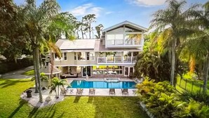 Uma casa de dois andares com piscina, rodeada por vegetação exuberante e palmeiras.