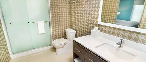 A bathroom with a glass shower enclosure, a toilet, a sink with a mirror, and patterned wall tiles.
