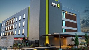 A modern hotel building with a sign reading "HOME 2 Suites by Hilton" and a covered outdoor area with seating. - Home2 Suites by Hilton Roseville Sacramento (Roseville)
