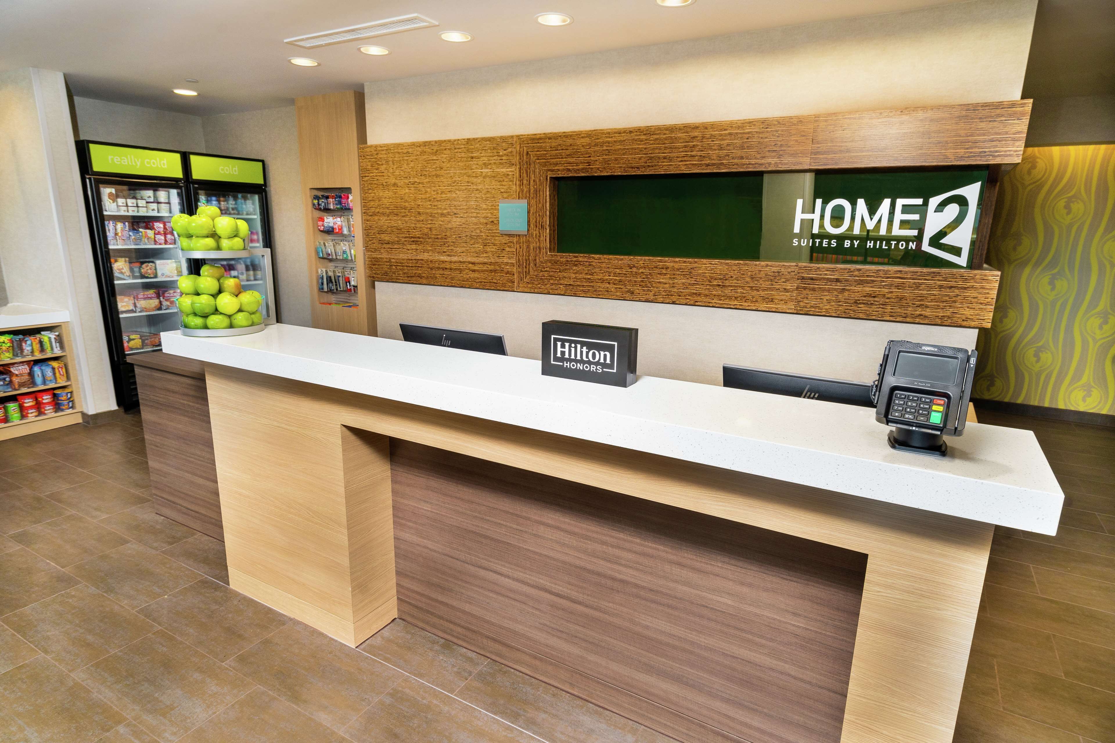 A hotel reception desk with a 'Hilton Honors' sign, a 'HOME2 Suites by Hilton' sign, and a self-service kiosk.