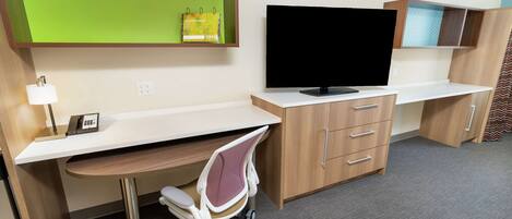 A modern office space with a desk, chair, television, and storage cabinets.