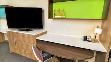 Hotelværelse med et fladskærms-tv, et skrivebord med lampe, telefon og en grøn skærm.