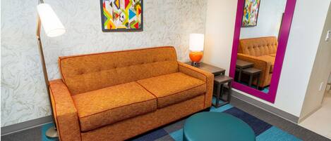 Una habitación moderna con sofá, un pouf redondo, una lámpara y un espejo.