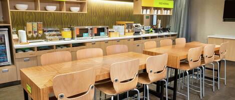 A dining area with a long wooden table and chairs, a buffet counter with various food items, and a sign that reads "inspired table".