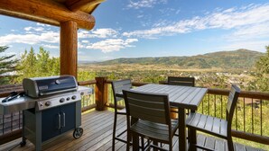 Una terraza de madera con una parrilla y una mesa, con vistas a un valle y colinas.