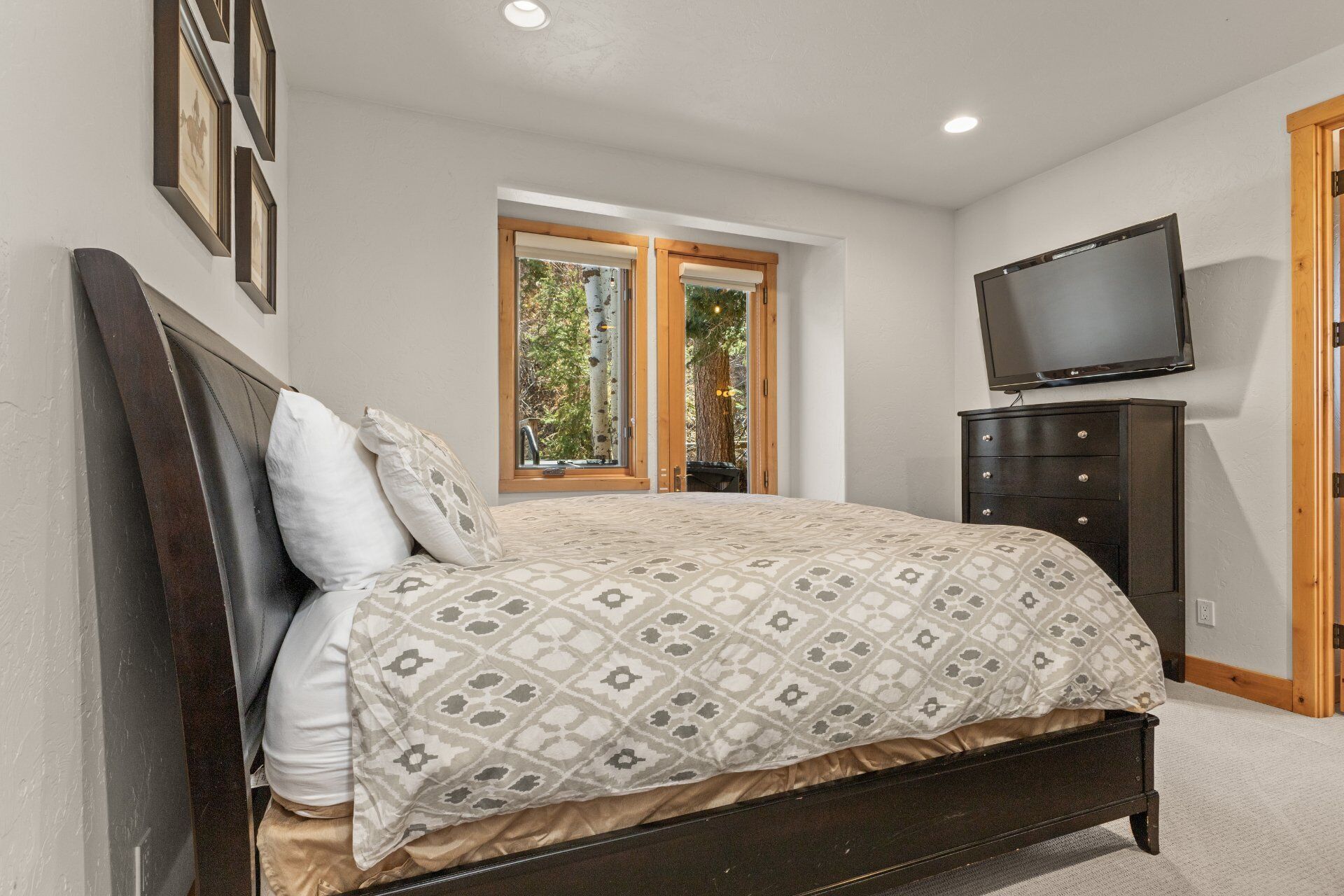 A bedroom with a bed, a dresser, a television, and a window with a view of trees.