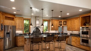 Una cocina moderna con armarios de madera, electrodomésticos de acero inoxidable, una isla central con taburetes altos e iluminación colgante.