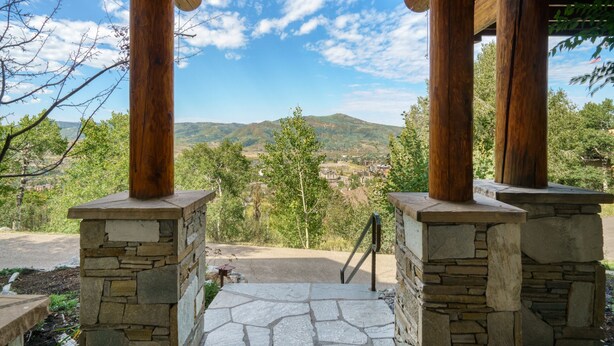 Una entrada empedrada con pilares de madera y vistas a un valle y montañas.