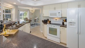 A modern kitchen with granite countertops, white cabinetry, a built-in microwave, a stove, and a refrigerator. - Gulf Access Waterfront, Pool with Heater, Friendly Neighborhood (Cape Coral)