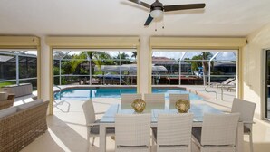 A poolside dining area with a table and chairs, a ceiling fan, and a view of the pool and outdoor area. - Gulf Access Waterfront, Pool with Heater, Friendly Neighborhood (Cape Coral)