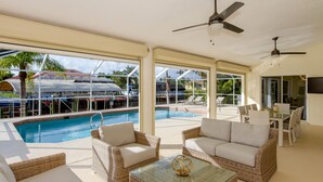 A poolside area with wicker furniture, a glass table, and a ceiling fan. - Gulf Access Waterfront, Pool with Heater, Friendly Neighborhood (Cape Coral)