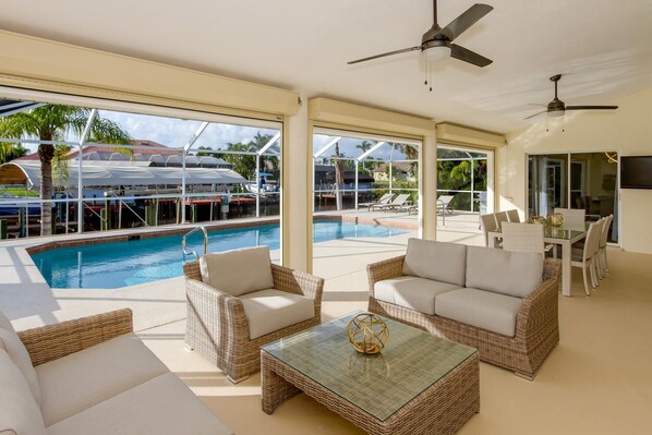 A poolside area with wicker furniture, a glass table, and a ceiling fan.