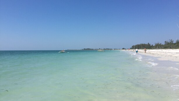 A beach with clear turquoise water, a sandy shore, and a few boats in the distance. - Gulf Access Waterfront, Pool with Heater, Friendly Neighborhood (Cape Coral)
