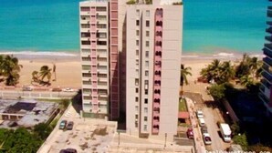 Een hoog hotel met meerdere verdiepingen, uitzicht op het strand en een parkeerplaats op de voorgrond.