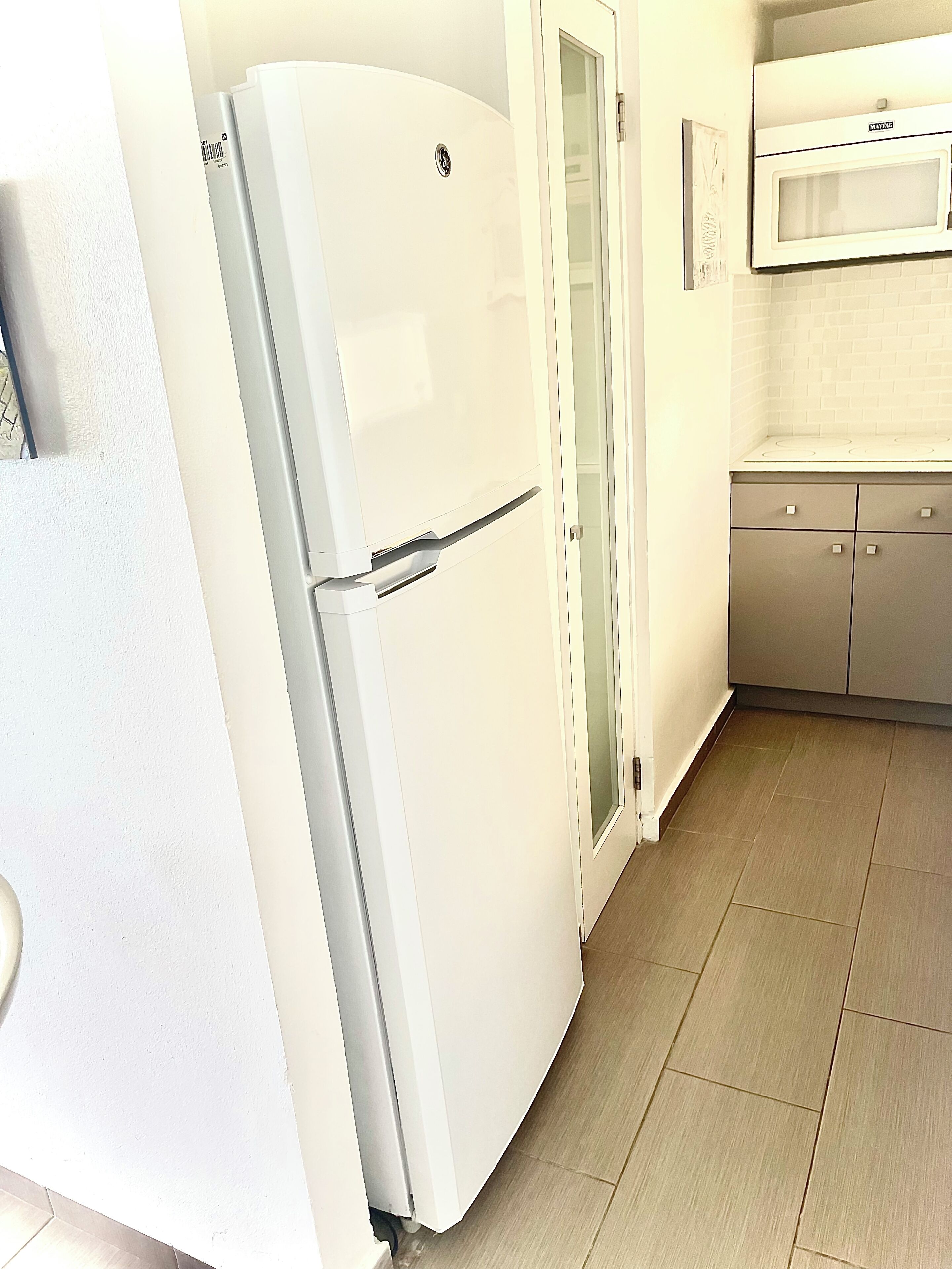 Una cocina compacta con un refrigerador blanco, un microondas y un mueble con cajones.