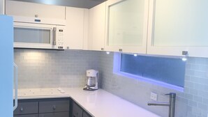Een moderne keuken met grijze kastjes, een wit aanrechtblad, een ingebouwde magnetron, een koffiezetapparaat en een spoelbak.