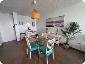A dining area with a glass table, white chairs, and a woven pendant light. - Too Good To Be True Beachfront Condo, New Modern Renovation. Free WIFI/Parking. (Isla Verde)