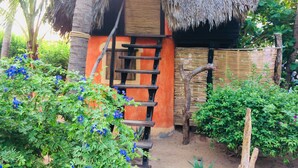 A rustic hut with a thatched roof, surrounded by lush greenery and flowering plants. - Posada Mexico (San Pedro Pochutla)