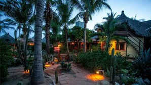 A tropical resort with palm trees, a thatched-roof building, and a paved pathway. - Posada Mexico (San Pedro Pochutla)