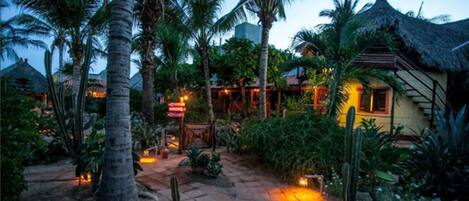 A tropical resort with palm trees, a thatched-roof building, and a paved pathway.