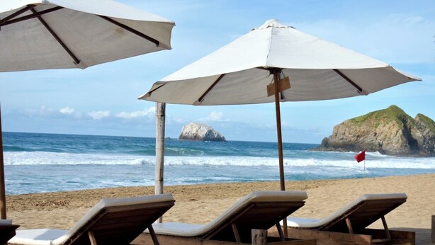 A beach with wooden lounge chairs and white umbrellas. - Posada Mexico (San Pedro Pochutla)