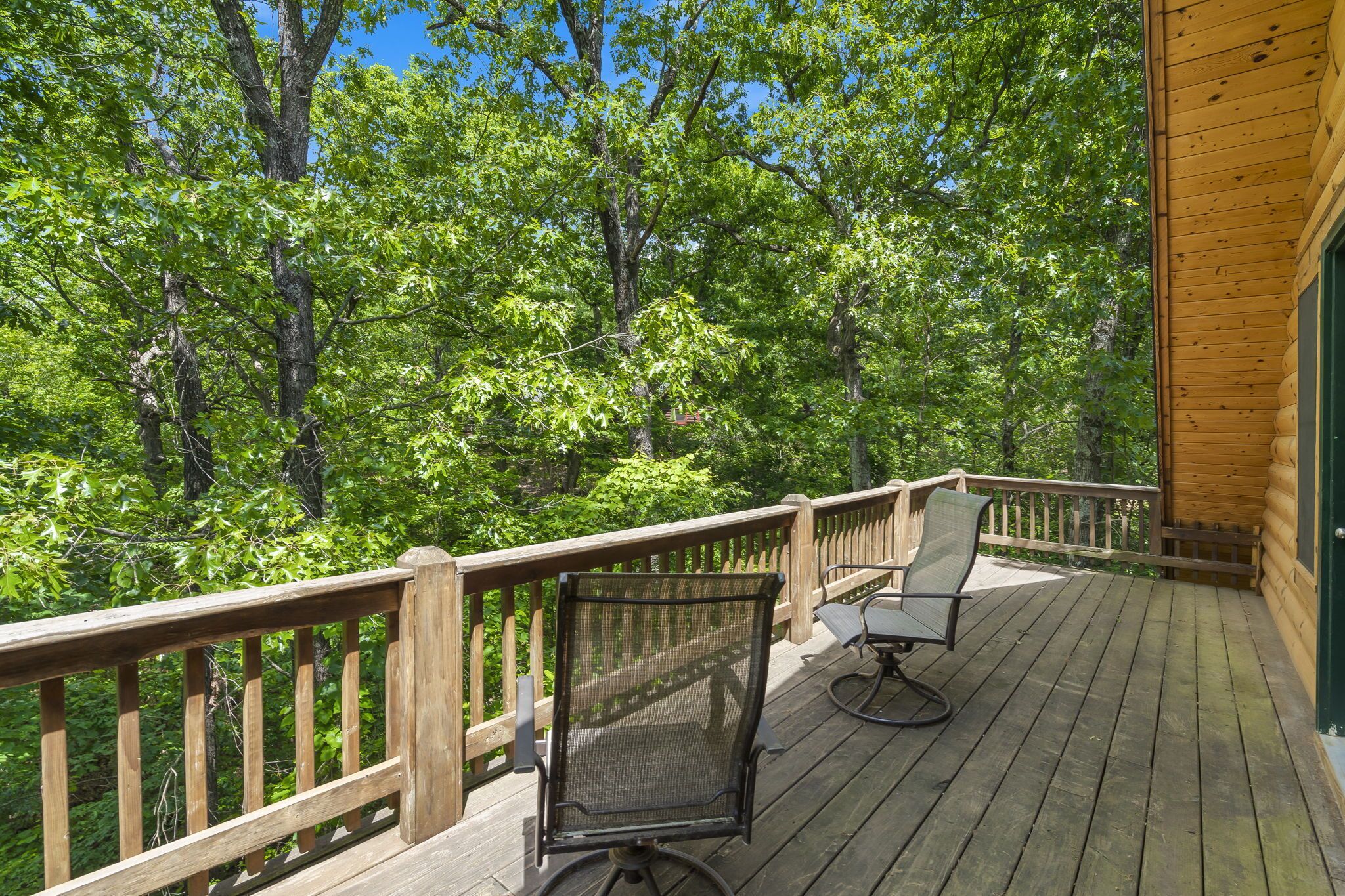 A wooden deck with two chairs and a railing overlooking a forest.
