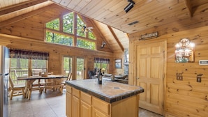 A cabin interior with a wooden interior, a kitchen area with a large island, and a dining area with wooden furniture. - Secluded Lodge w HotTub_Loft w Games_Near Big Cedar Trophy Buck_Pet Friendly_Car Charger_Slide (Ridgedale)