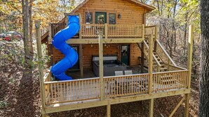 A wooden cabin with a spiral slide, a hot tub, and a deck. - Secluded Lodge w HotTub_Loft w Games_Near Big Cedar Trophy Buck_Pet Friendly_Car Charger_Slide (Ridgedale)