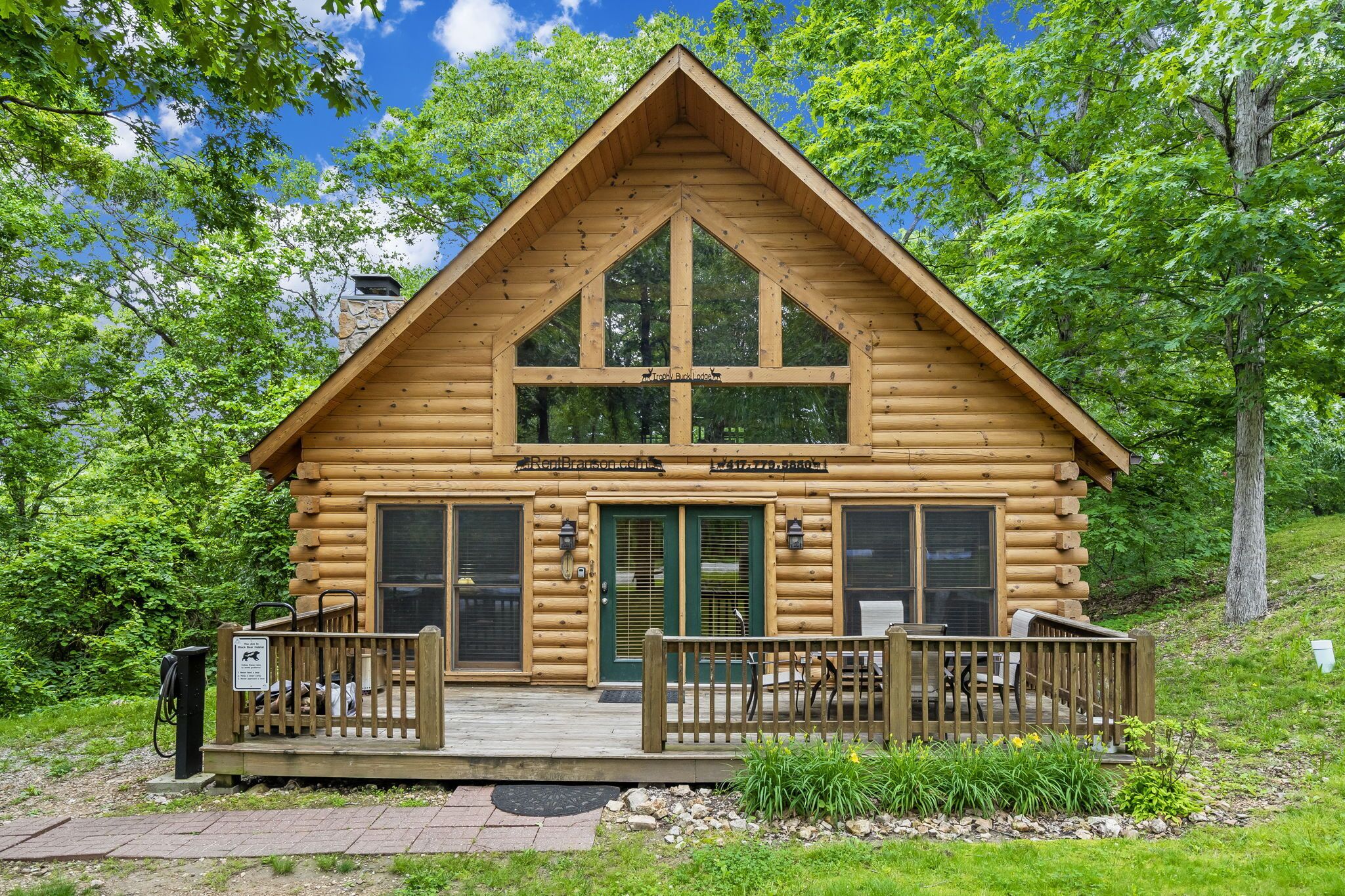 A log cabin with a wooden deck, large windows, and a stone chimney.