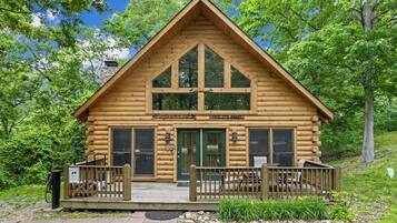 A log cabin with a wooden deck, large windows, and a stone chimney.