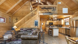 A cabin interior with a living room, kitchen, and a staircase leading to a loft. - Secluded Lodge w HotTub_Loft w Games_Near Big Cedar Trophy Buck_Pet Friendly_Car Charger_Slide (Ridgedale)