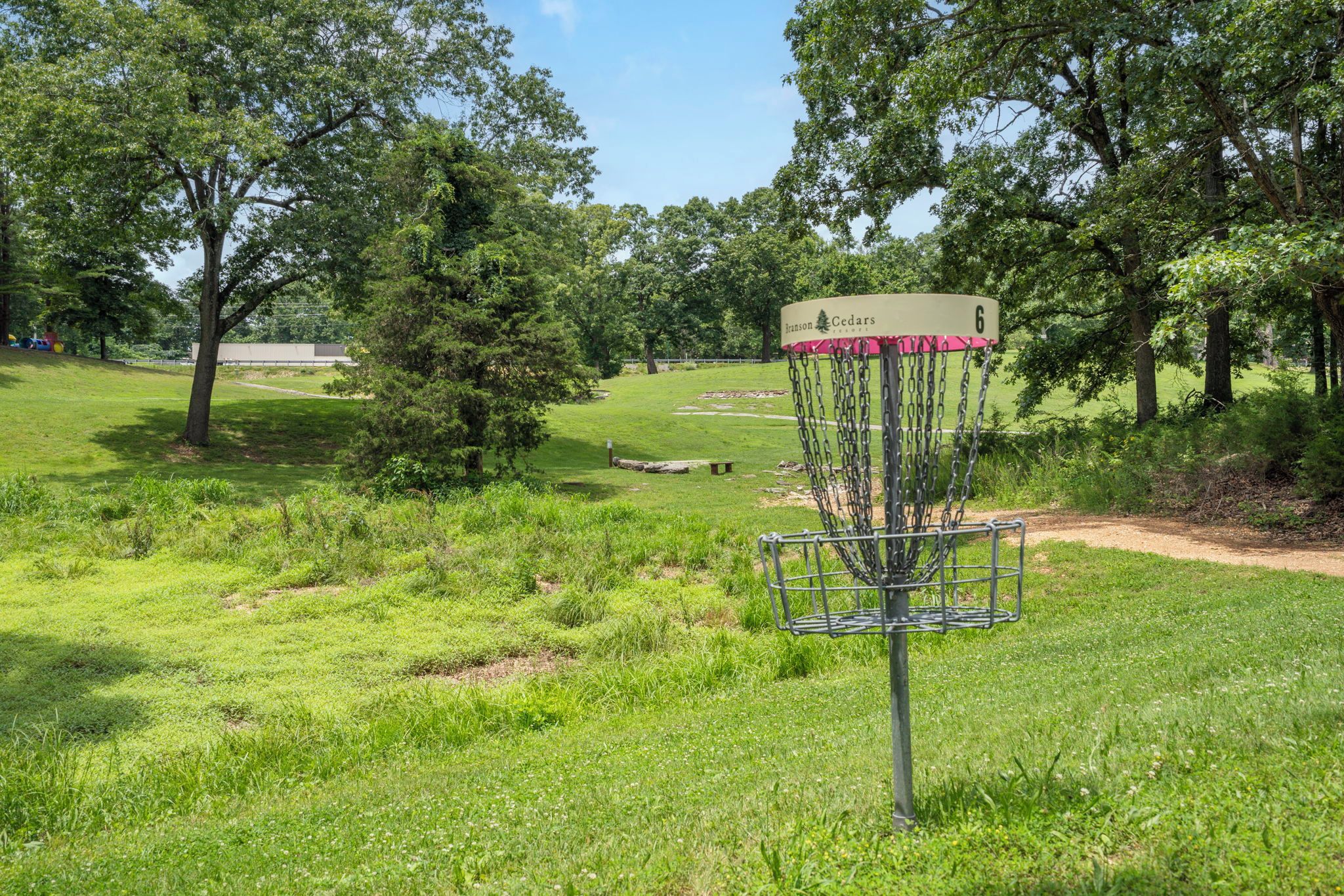 A disc golf basket with a sign, surrounded by a grassy field with trees.