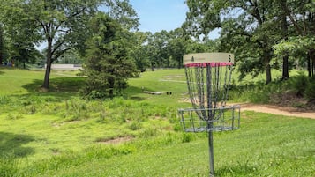 A disc golf basket with a sign, surrounded by a grassy field with trees.